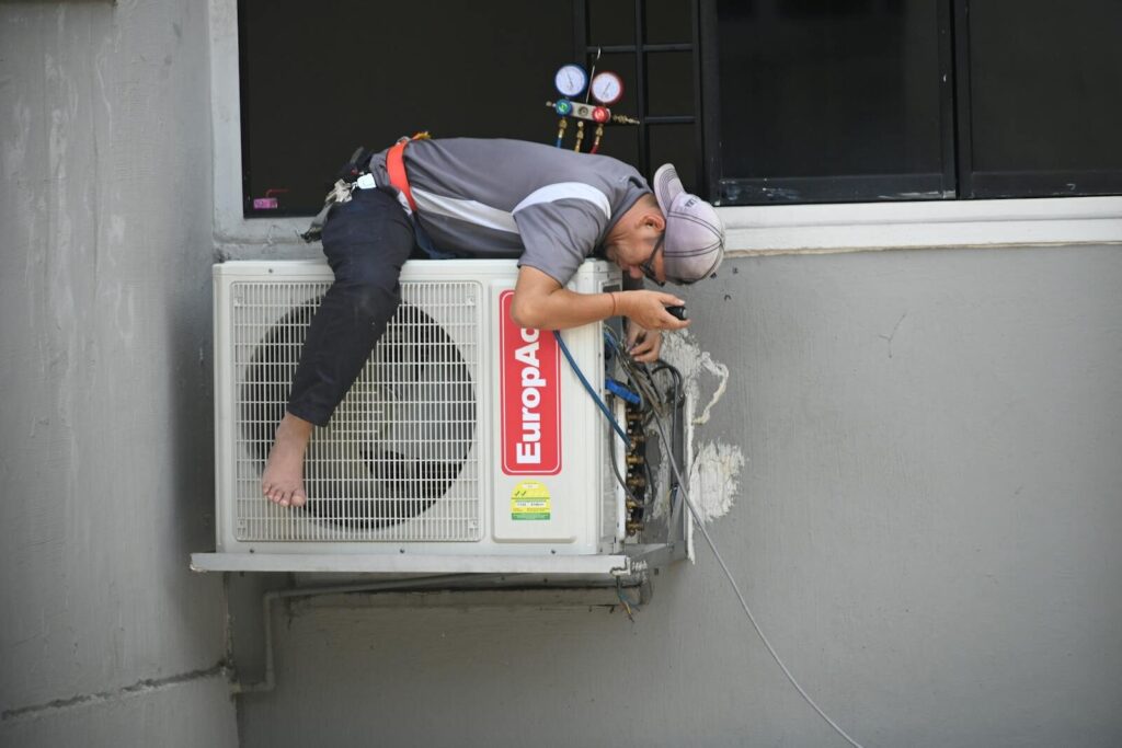 A technician skillfully repairing an outdoor air conditioning unit mounted on a building wall.